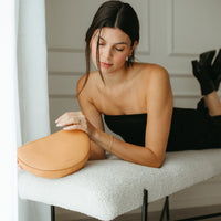 Woman sitting on a chair holding a yellow handbag in a minimalistic room.