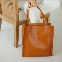 Person holding a brown leather tote bag in a minimalistic setting