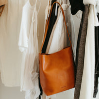 Brown leather handbag hanging on a rack with clothes