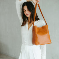 Woman holding a brown leather bag against a plain background