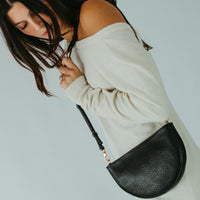 Woman holding a black leather handbag against a light blue background