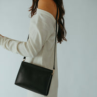 Woman wearing a white off-shoulder dress with a black handbag on a plain background