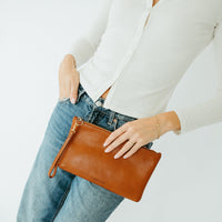 Person holding a brown leather clutch with a plain background