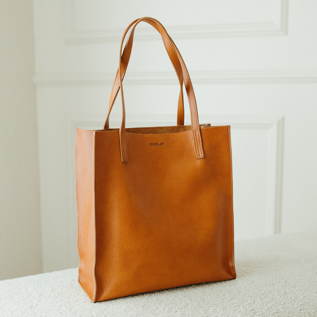 Brown leather tote bag on a textured surface with a neutral background