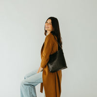 Woman in a mustard yellow coat holding a black bag against a white background