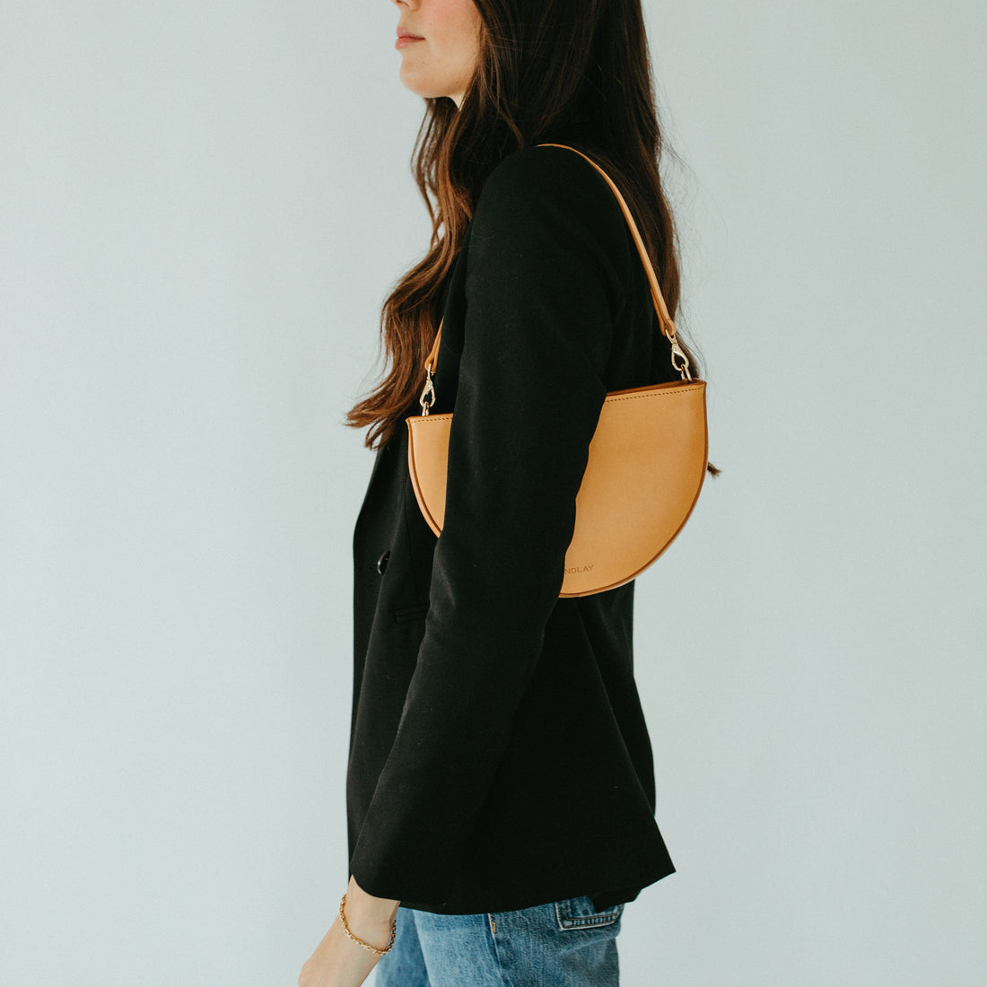 Woman carrying a tan shoulder bag against a plain background