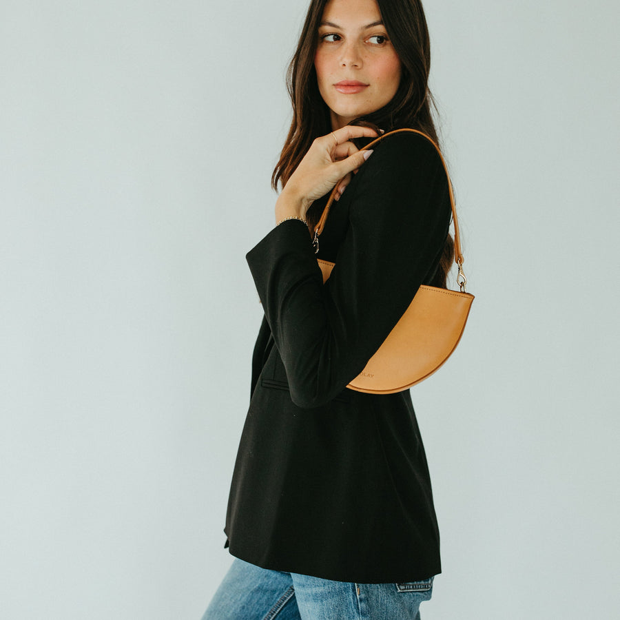Woman holding a tan leather handbag against a plain background