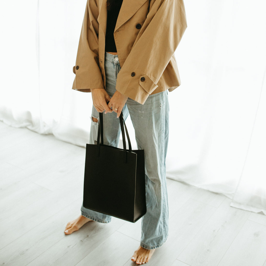 Woman wearing a beige coat and holding a black bag in a minimalistic setting