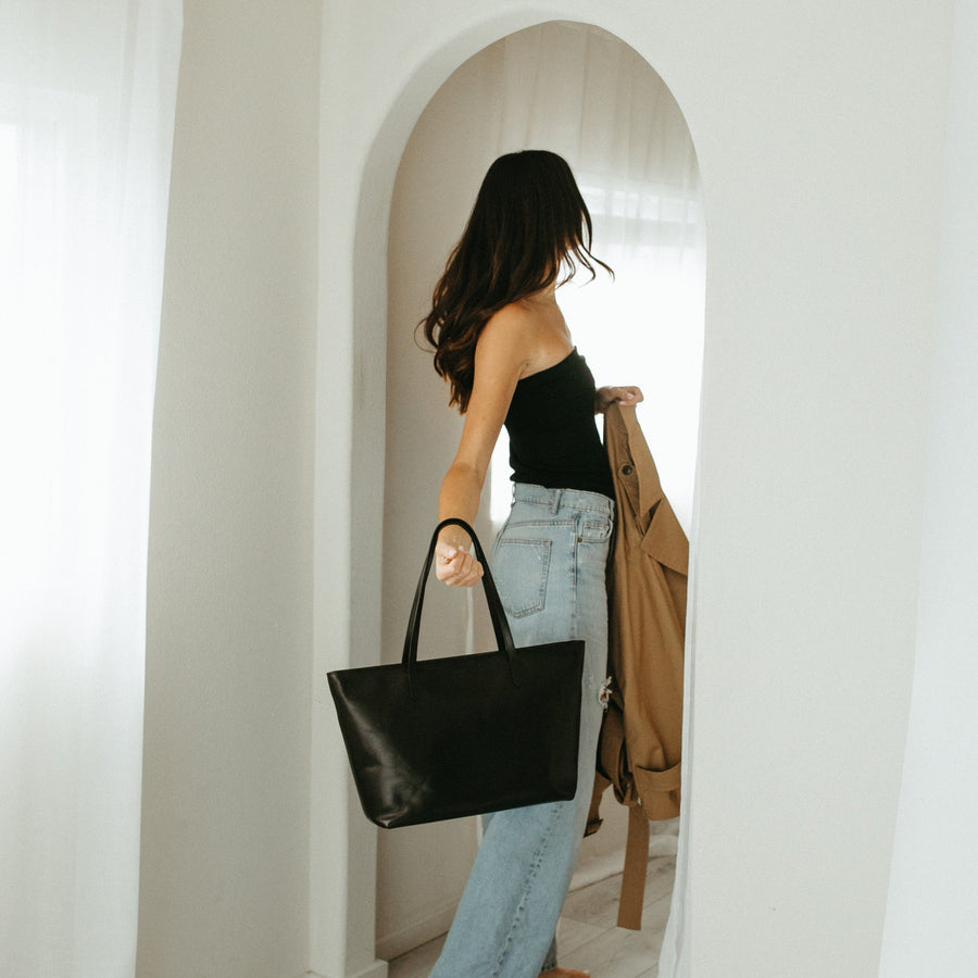 Woman holding a black handbag in a room with white walls and a wooden floor.
