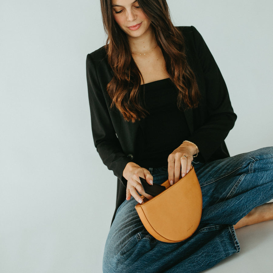 Woman holding a brown leather clutch against a plain background