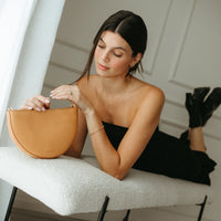 Woman sitting on a bench holding a tan handbag, wearing a black dress.