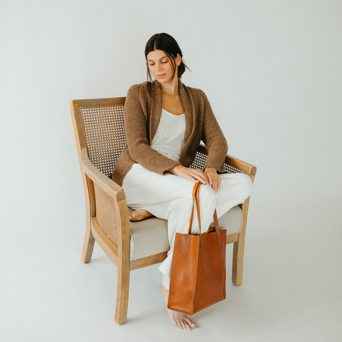 Woman sitting on a chair holding a brown leather bag against a white background