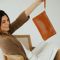 Woman sitting on a couch holding a brown leather handbag.
