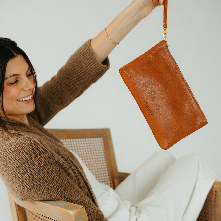 Woman sitting on a couch holding a brown leather handbag.