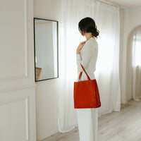 Woman holding a red tote bag in a room with white walls and curtains.