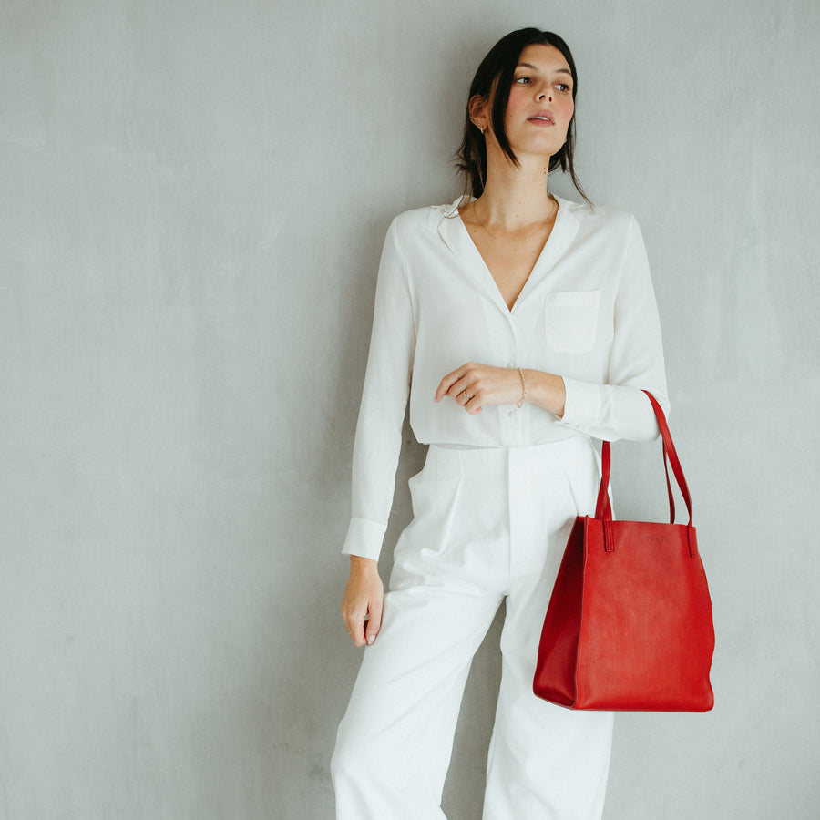 Woman in white outfit holding a red bag against a plain background