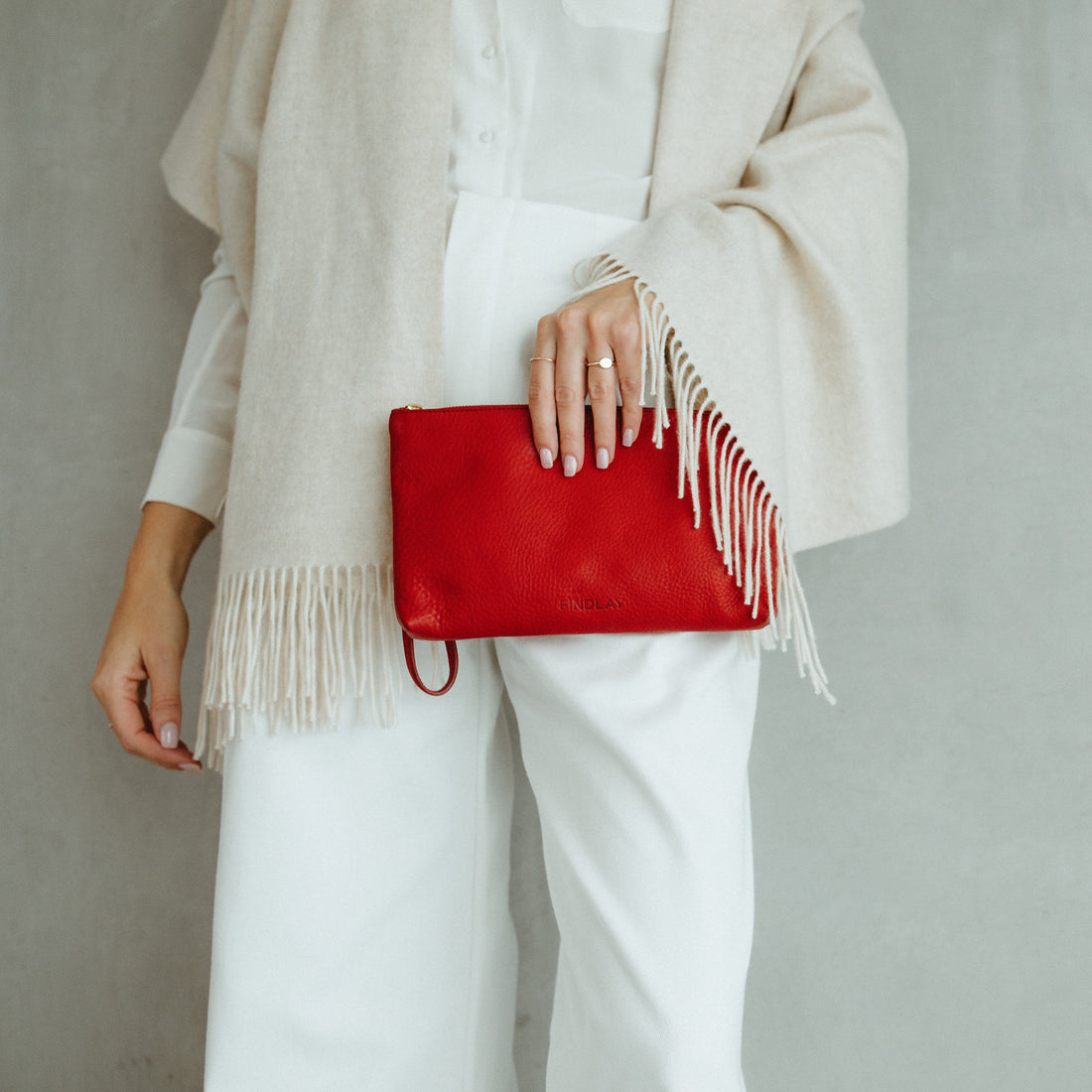 Person holding a red clutch with white fringe against a plain background