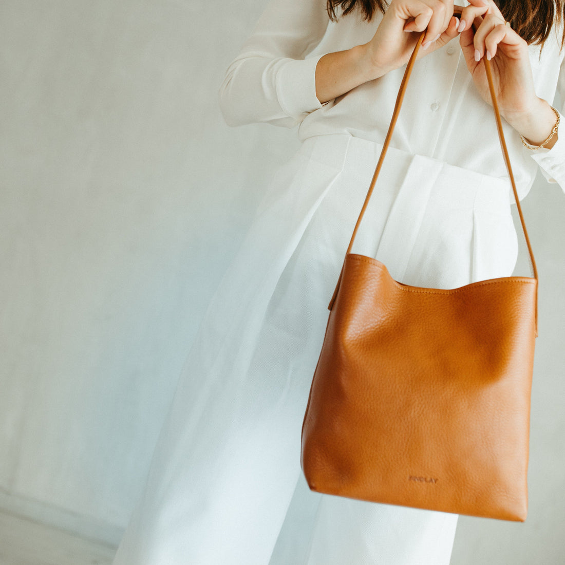 Person holding a brown leather bag against a neutral background
