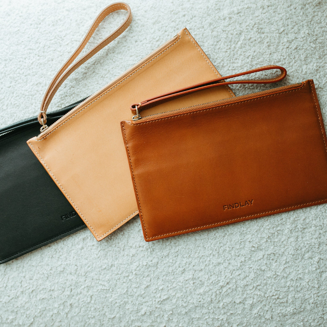 Three leather bags in black, beige, and brown on a textured surface