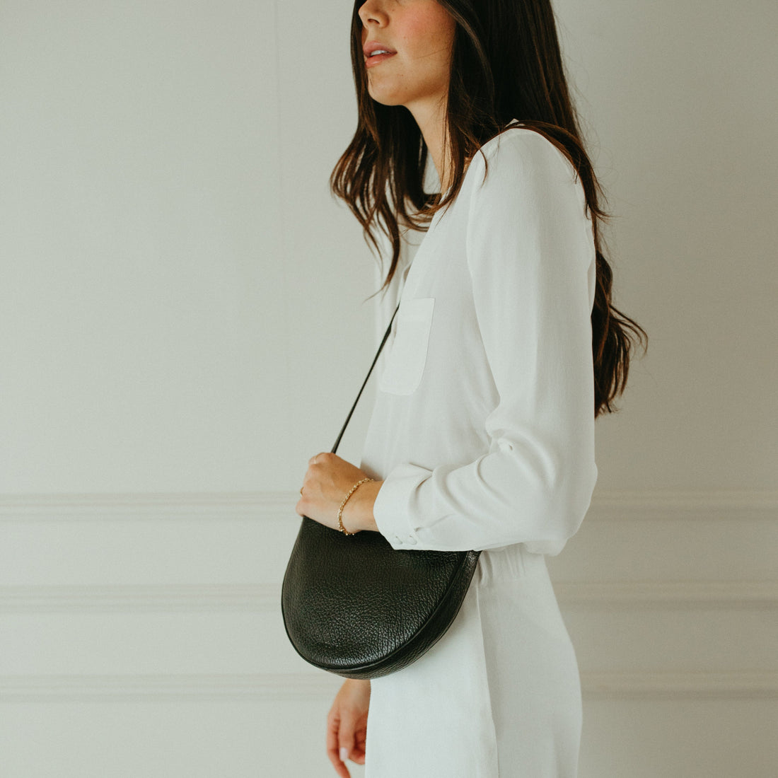 Woman in a white outfit holding a black handbag against a plain background