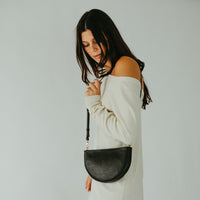 Woman holding a black handbag against a plain background