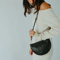 Woman holding a black handbag against a plain background