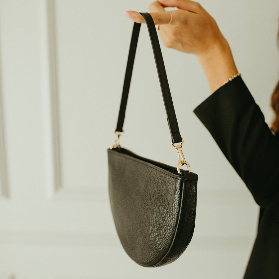 Person holding a black handbag against a neutral background