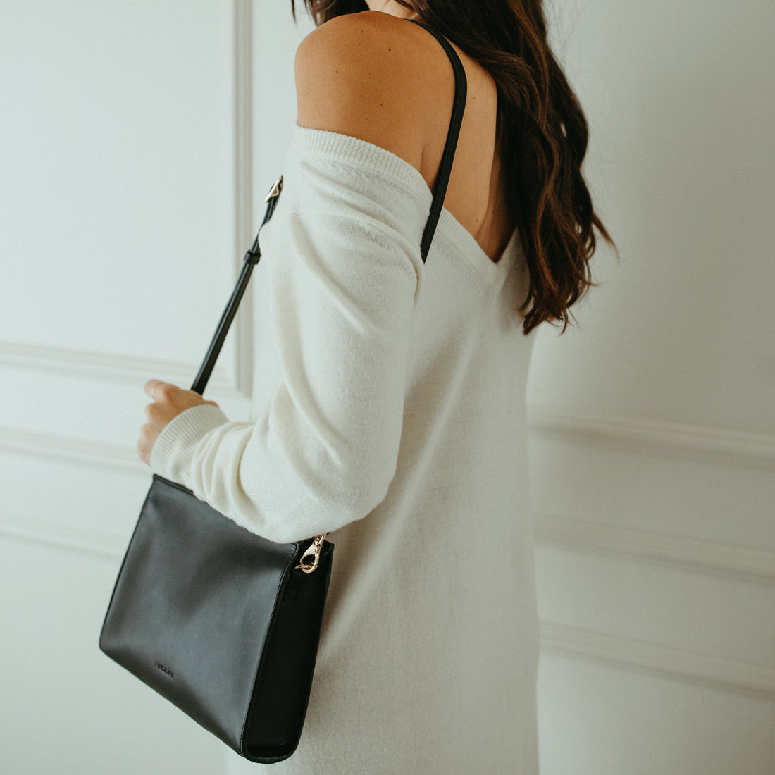 Woman holding a black handbag against a white wall