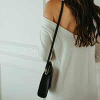 Woman wearing a white off-shoulder top with a black handbag against a light background