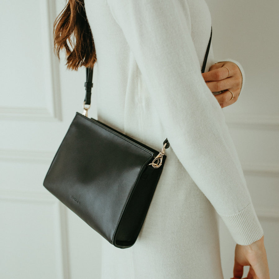 Person holding a black handbag against a neutral background