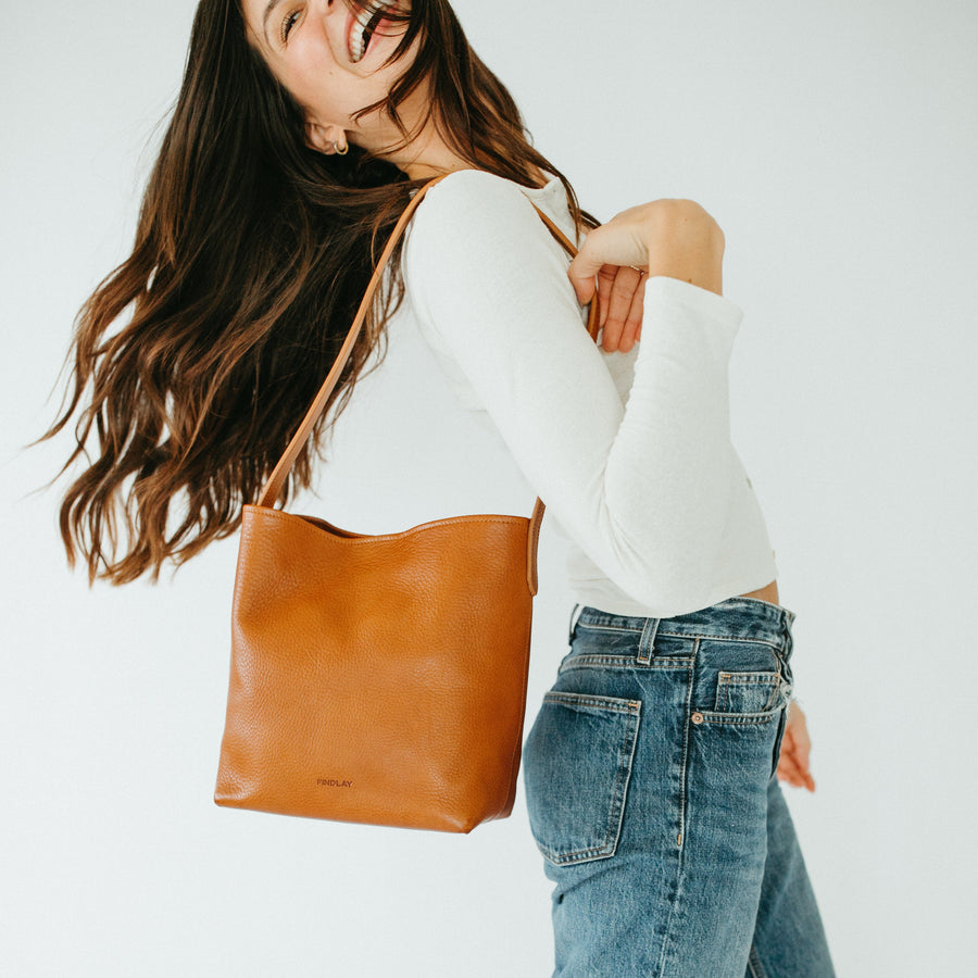 Woman holding a brown leather tote bag against a white background