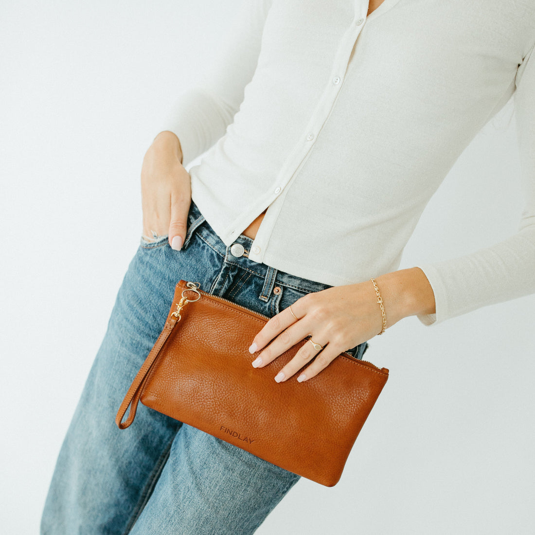 Person holding a brown leather clutch with a plain background