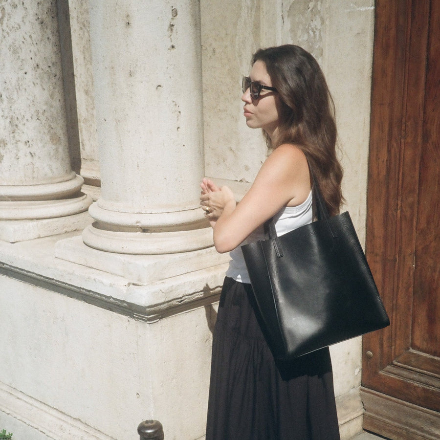 Woman holding a black tote bag against a stone building background